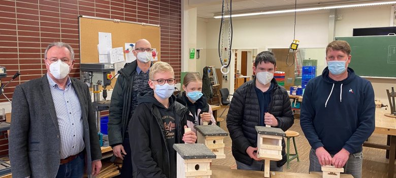 Drei Lehrer, zwei Schüler und eine Schülerin stehen in einem Werkraum und halten selbstgebaute Nistkästen in der Hand.
