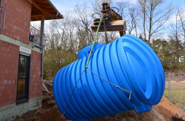 Ein Bagger lässt eine blaue Regenwasserzisterne in den Boden.