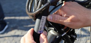 Eine Person, von der nur die Hände zu sehen sind, klebt ein Nummernschild-Aufkleber an ein Fahrrad. 