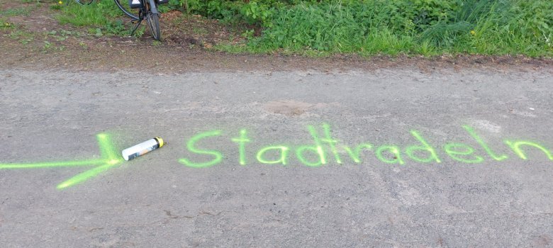 SR-Markierungen Auf einer Straße steht, mit grüner Farbe gesprüht, das Wort Stadtradeln.