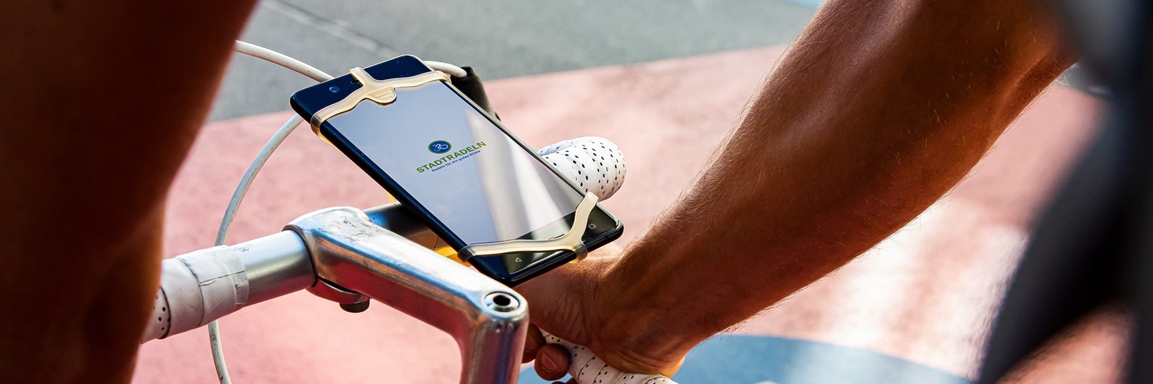 Ein Fahrradfahrer fährt auf dem Radweg. An seinem Lenker ist ein Smartphone angebracht, auf dem die Stadtradeln-App zu erkennen ist.