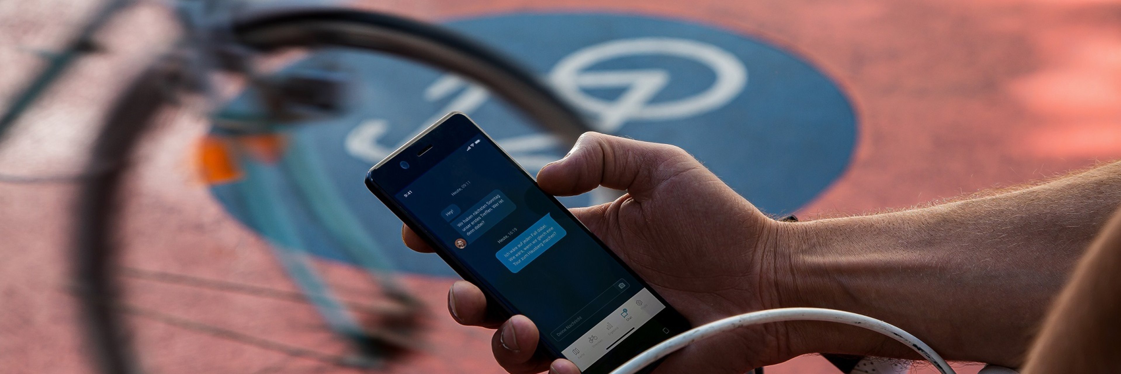 Ein Fahrrad auf einem Radweg. Der Fahrer macht eine Pause und hält sein Smartphone in der Hand. 