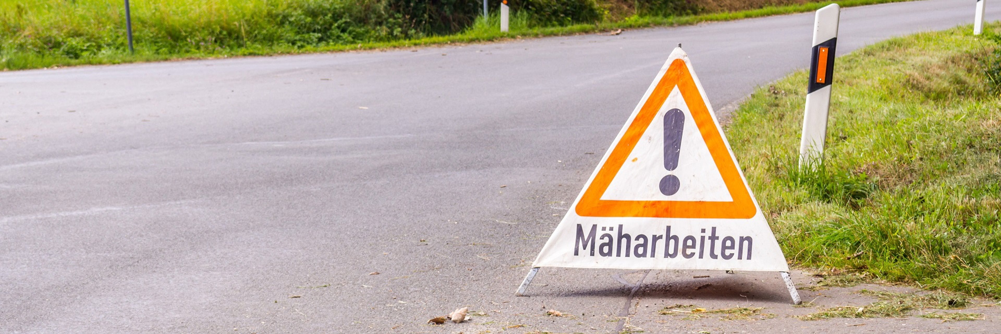 Ein Warnschild an der Straße weist auf die Mäharbeiten hin. 