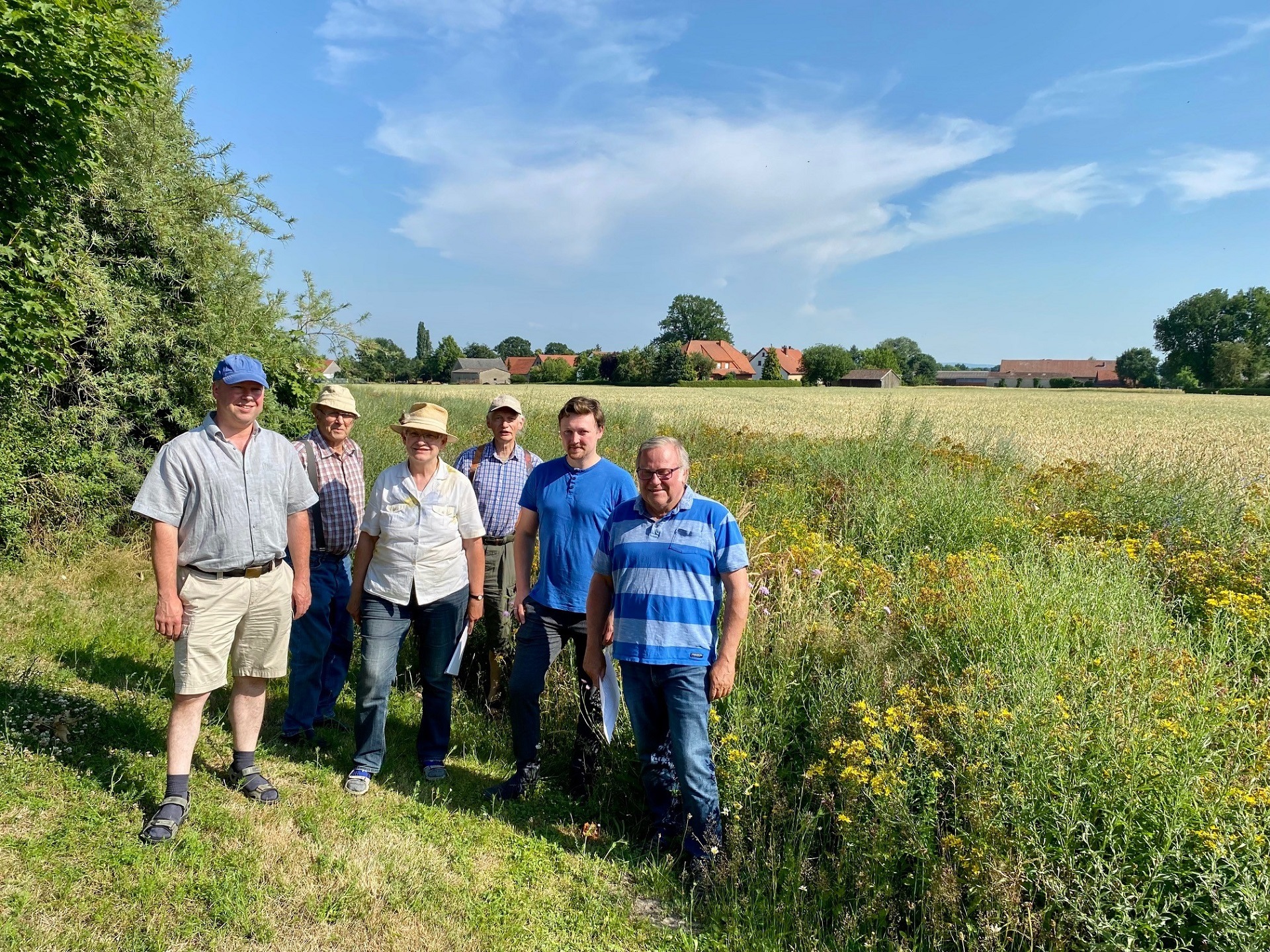 Blühflächen_1 Eine Gruppe von Frauen und Männern steht in sommerlicher Kleidung vor eine Blühwiese.