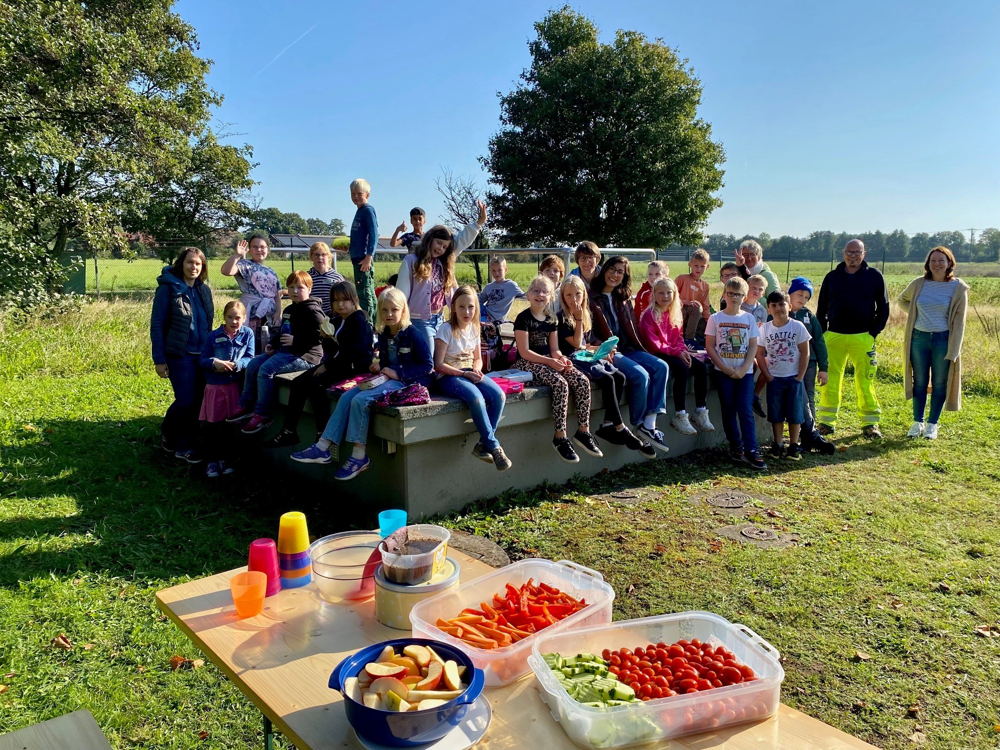 WW-Besuch 1 Viele Kinder, die auf einer Empore im Freien sitzen und dabei Pausenbrote und Obst essen.
