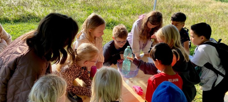 Kinder, die um einen Tische herum stehen und Experimente mit einer Wasserflasche machen.