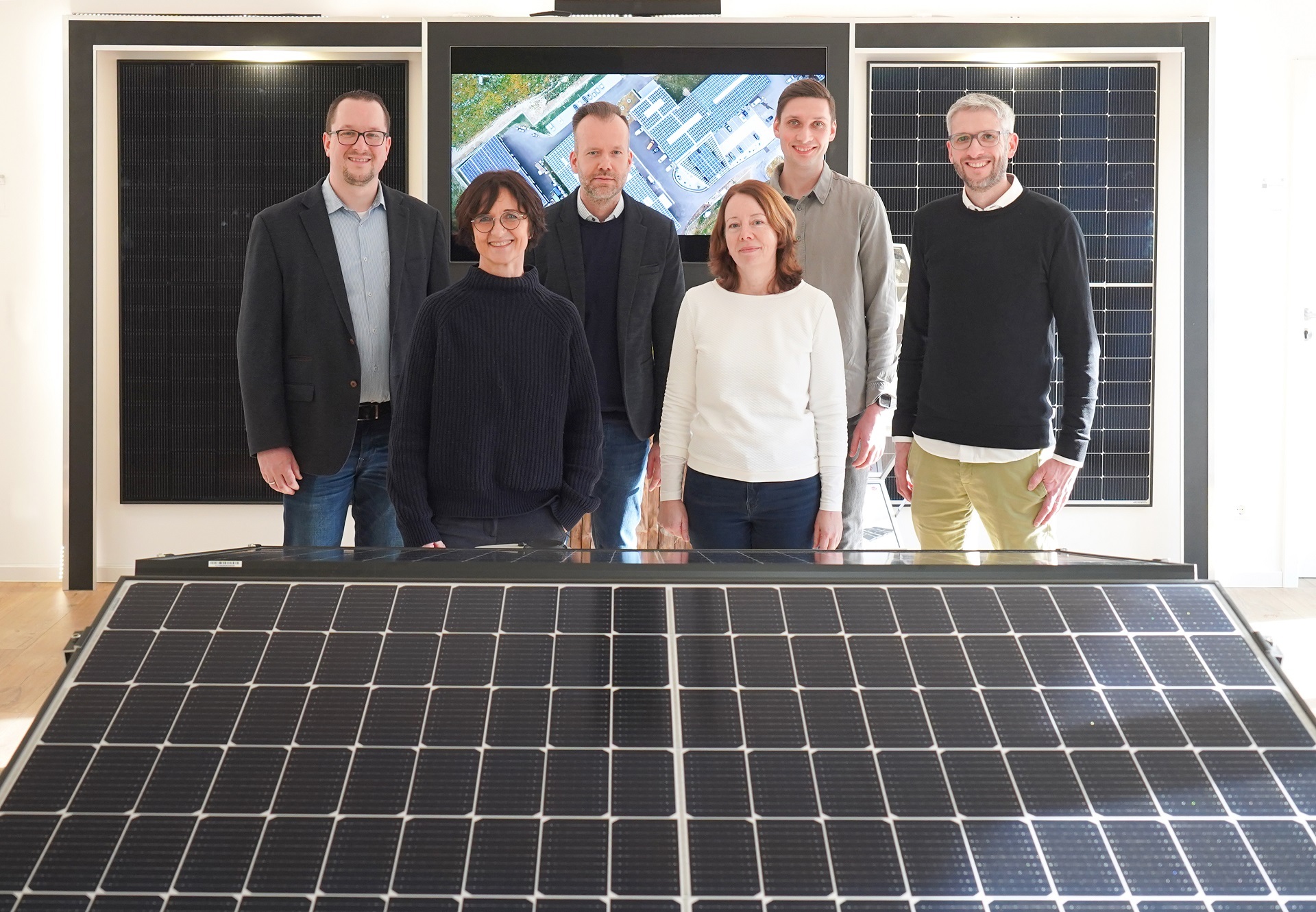 Infoveranstaltung Solar 2023 6 Personen - vier Männer, zwei Frauen - die hinter einem Solarpanel stehen und in die Kamera lächeln.