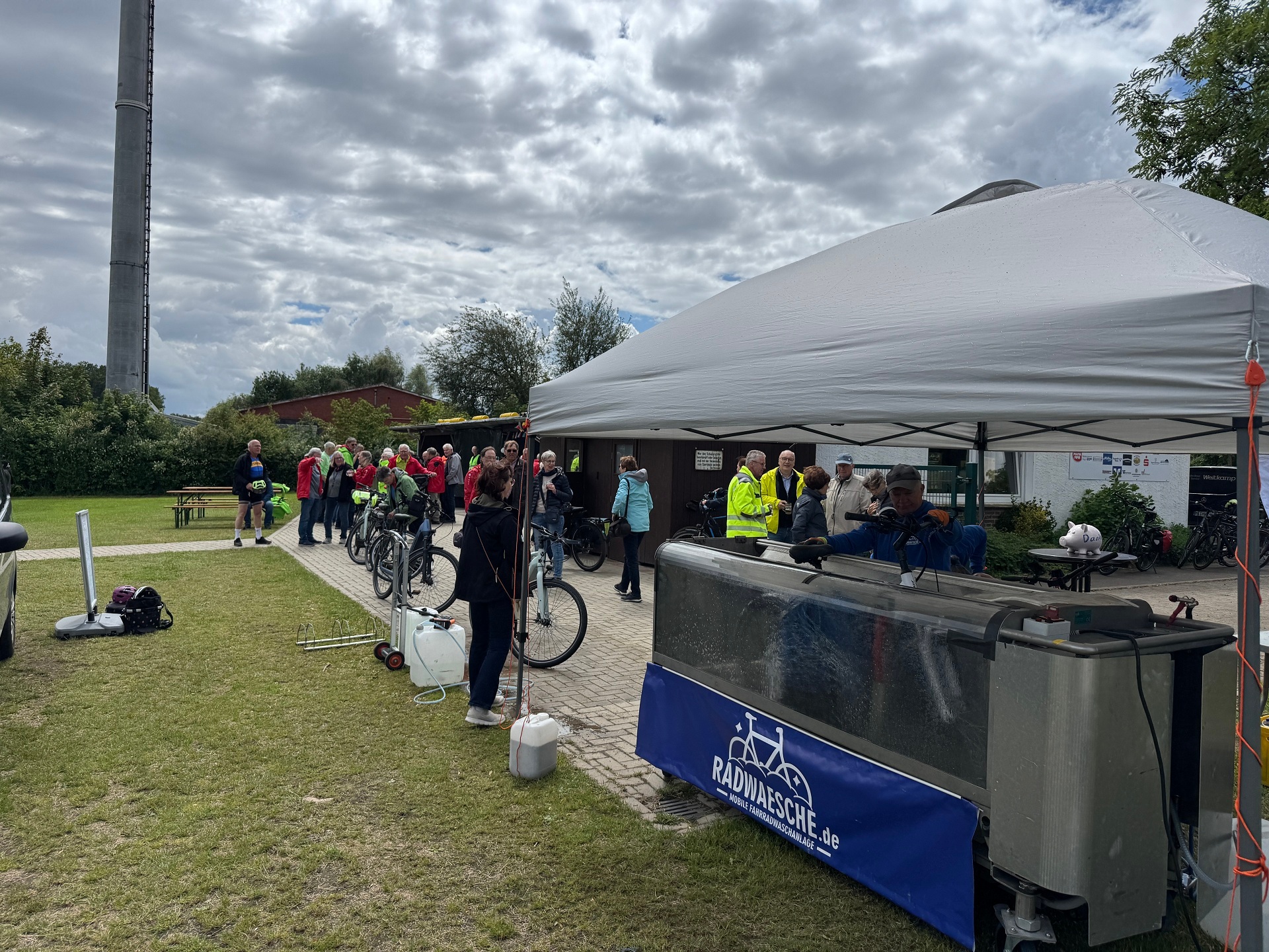 Mehrere Teilnehmerinnen und Teilnehmer des STADTRADELN-Abschlusstages warten mit ihren Fahrrädern vor einer mobilen Fahrradwaschanlage auf dem Sportplatz in Levern. Unter einem weißen Pavillon werden Fahrräder gereinigt, während sich weitere Gäste auf dem Veranstaltungsgelände austauschen. Die Waschanlage gehörte zu den beliebtesten Angeboten des Aktionstages.