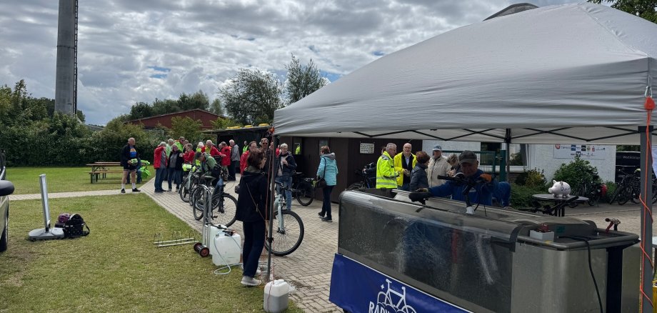 STADTRADELN-Abschluss 2026 Mehrere Teilnehmerinnen und Teilnehmer des STADTRADELN-Abschlusstages warten mit ihren Fahrrädern vor einer mobilen Fahrradwaschanlage auf dem Sportplatz in Levern. Unter einem weißen Pavillon werden Fahrräder gereinigt, während sich weitere Gäste auf dem Veranstaltungsgelände austauschen. Die Waschanlage gehörte zu den beliebtesten Angeboten des Aktionstages.