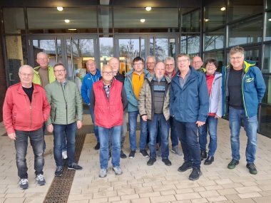 Ein Gruppenfoto mit 13 Männern und einer Frau vor dem  Eingang eines Schulgebäudes.